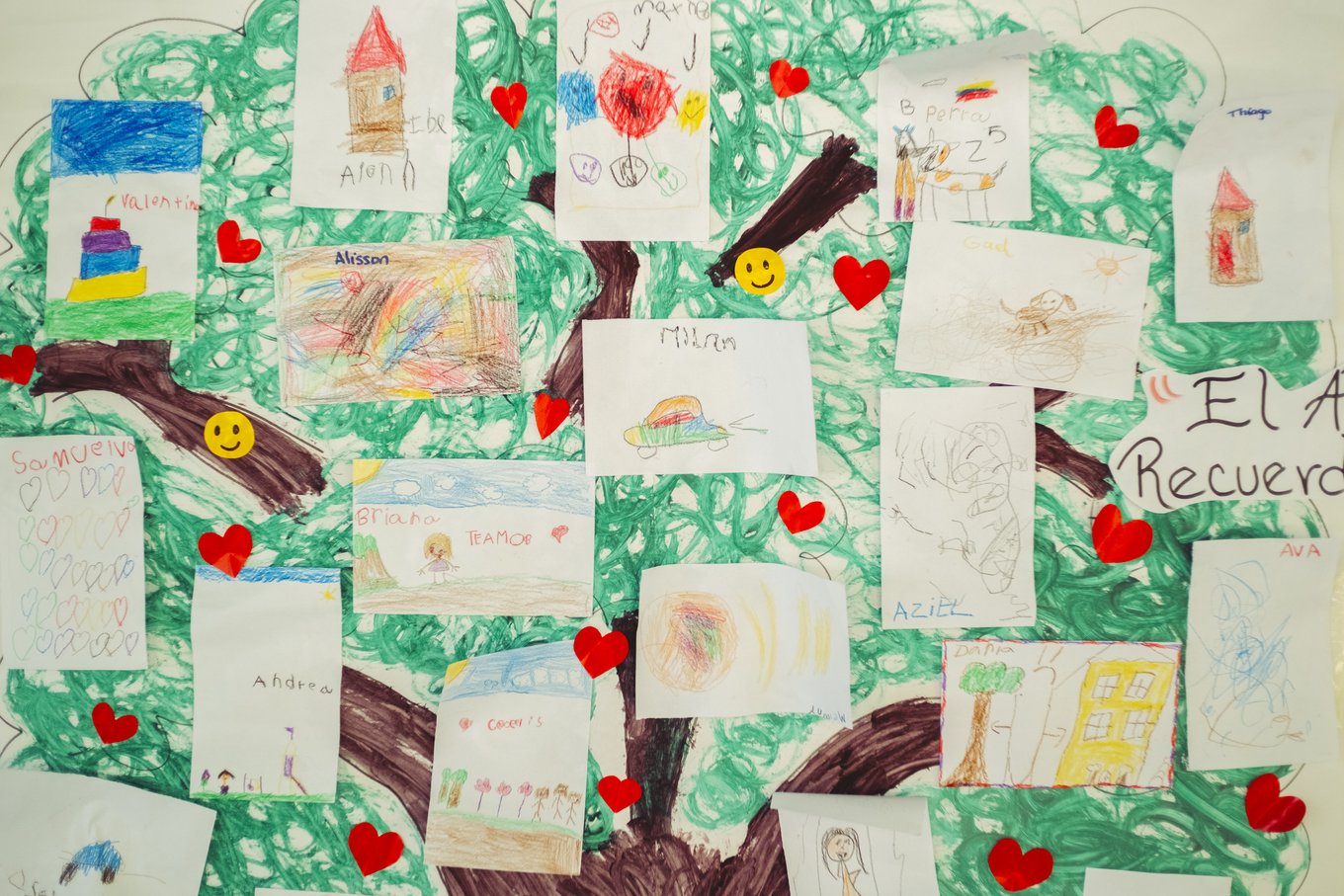 Dibujos de niños pegados en un árbol pintado en papel, con corazones rojos